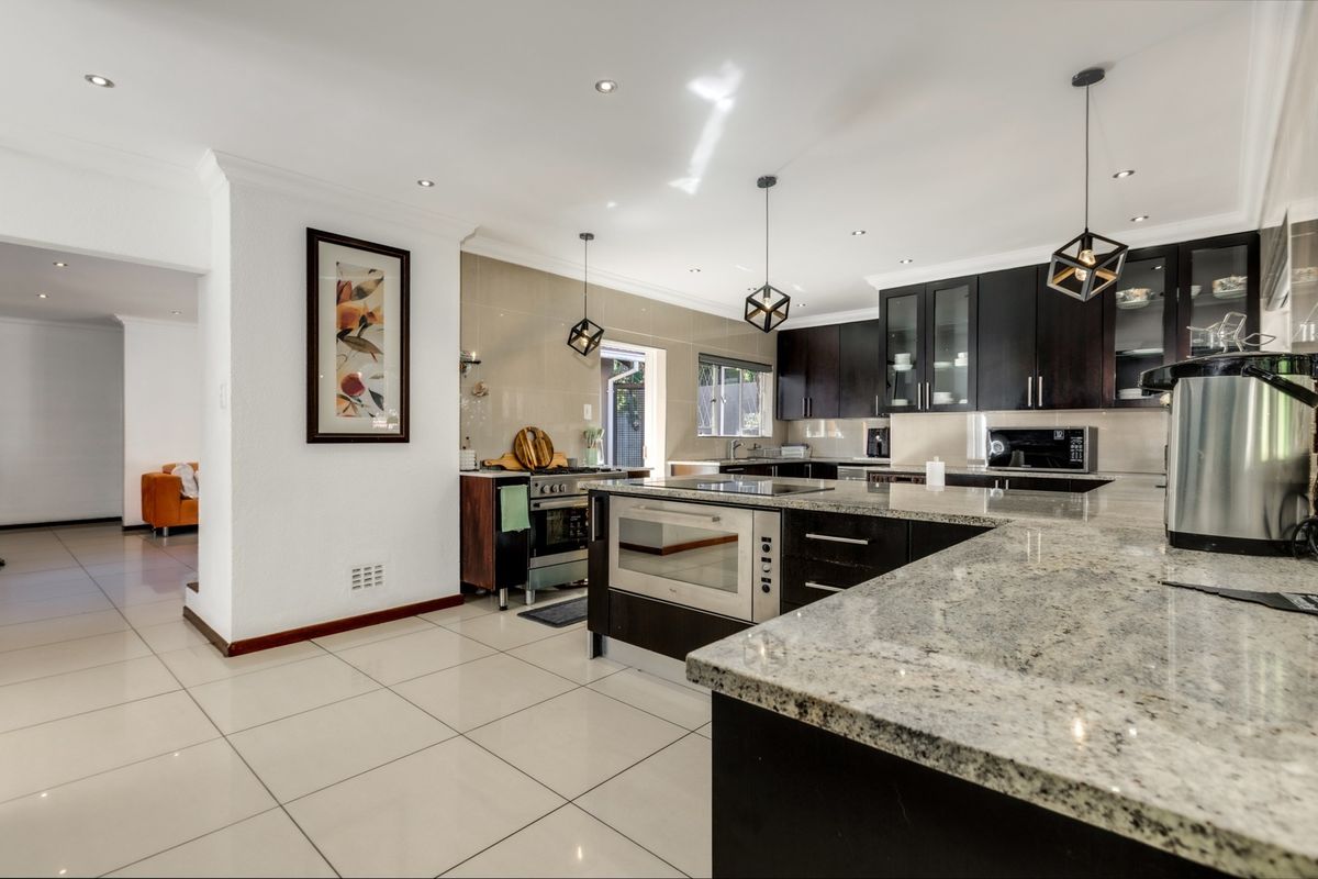 Modern kitchen featuring dark cabinetry, granite countertops, built-in appliances, and stylish pendant lighting, seamlessly flowing into the adjacent living area.