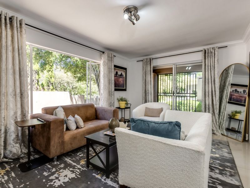 Bright living room featuring large windows, sliding glass doors with security gate, tiled flooring, and crown molding, offering natural light and garden access.