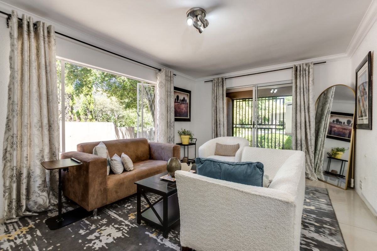 Bright living room featuring large windows, sliding glass doors with security gate, tiled flooring, and crown molding, offering natural light and garden access.