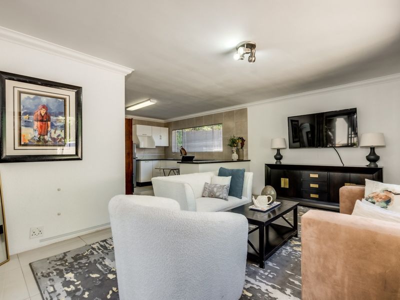 An open-plan living area featuring tiled floors, coving, and a connected kitchen space with built-in cabinetry and countertops.