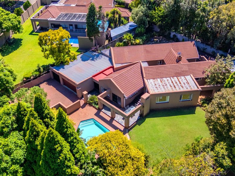 Aerial view of a residential property featuring a tiled roof, swimming pool, paved driveway, and a covered patio area set within a landscaped garden.