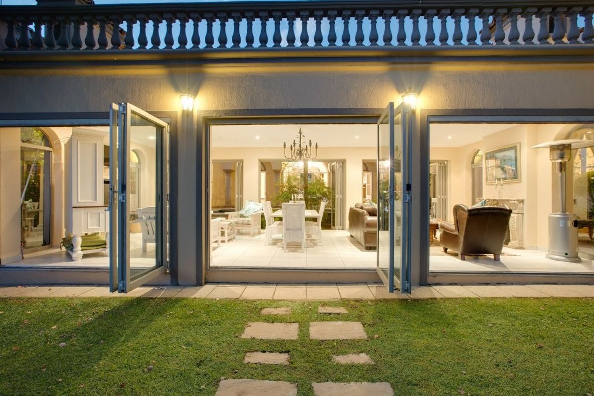 Rear view of the property featuring expansive folding glass doors opening onto a manicured lawn with a classic stone balustrade above.