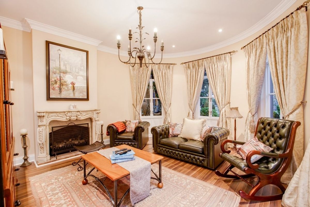A classic living room featuring a curved wall, ornate stone fireplace, hardwood flooring, and elegant coved ceilings with a decorative chandelier.