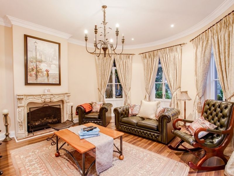 A classic living room featuring a curved wall, ornate stone fireplace, hardwood flooring, and elegant coved ceilings with a decorative chandelier.