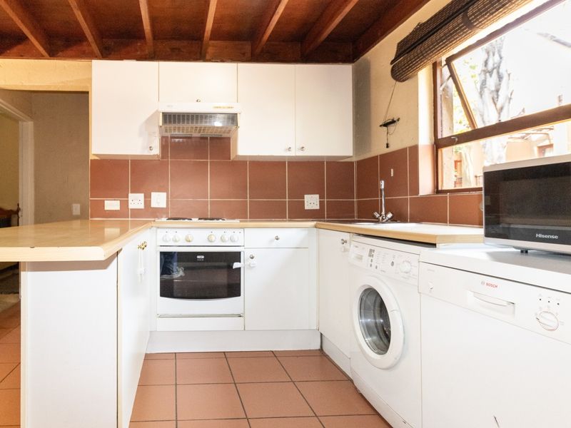 A functional kitchen featuring white cabinetry, tiled backsplash, built-in oven, hob, and exposed timber ceiling beams, offering a practical layout for daily use.
