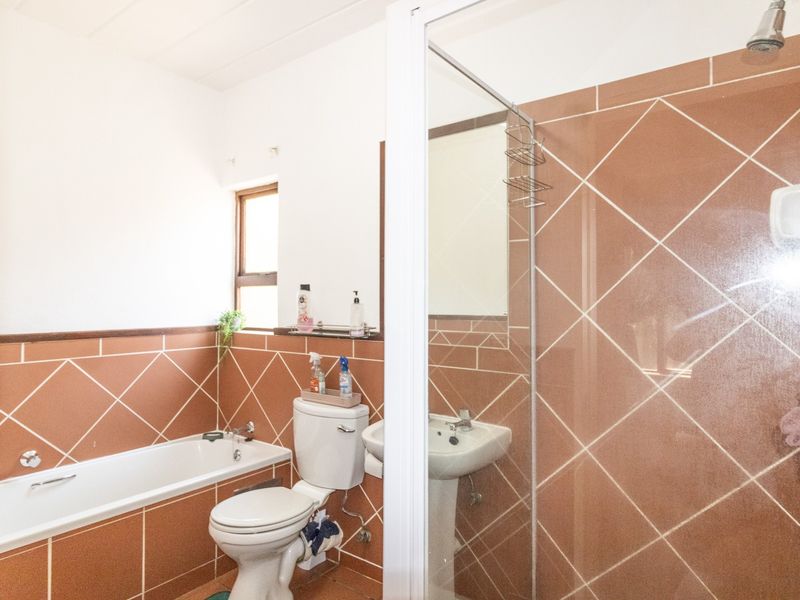A functional bathroom featuring a bathtub, pedestal sink, toilet, and a separate shower enclosure with brown diamond-patterned wall tiles.