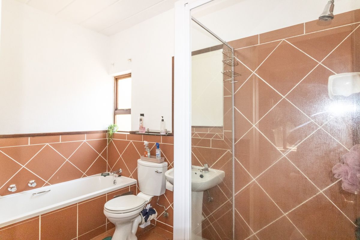 A functional bathroom featuring a bathtub, pedestal sink, toilet, and a separate shower enclosure with brown diamond-patterned wall tiles.