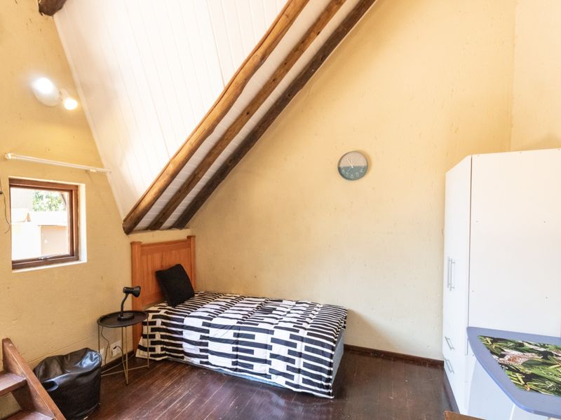 A cozy attic-style bedroom featuring exposed timber rafters, sloped ceilings, and timber flooring, offering a unique architectural character.