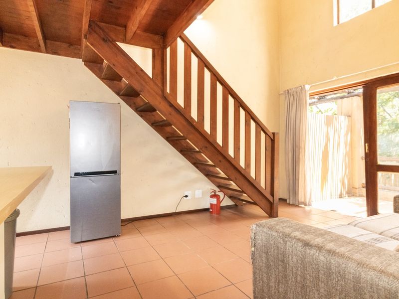 Open-plan living area featuring a wooden staircase, tiled flooring, and direct access to an outdoor patio through a sliding glass door.