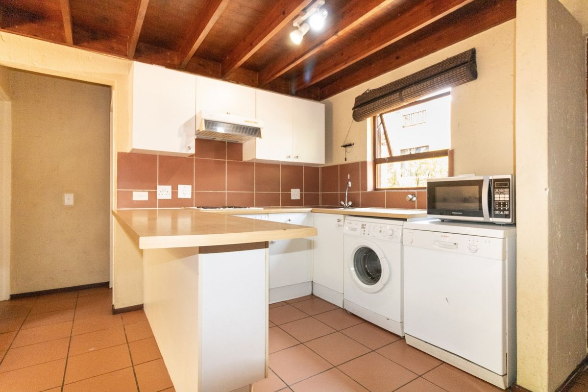 Functional kitchen featuring white cabinetry, laminate countertops, tiled backsplash, and exposed timber ceiling beams, providing a practical layout with integrated appliance space.