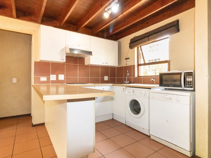 Functional kitchen featuring white cabinetry, laminate countertops, tiled backsplash, and exposed timber ceiling beams, providing a practical layout with integrated appliance space.