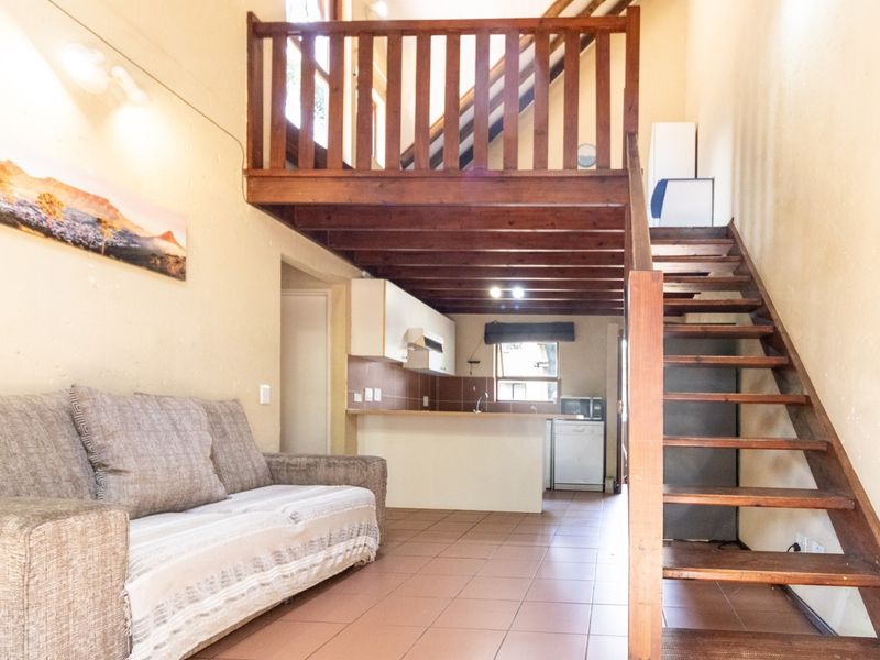 Open-plan living area featuring a kitchen with tiled backsplash and a wooden staircase leading to a mezzanine level.