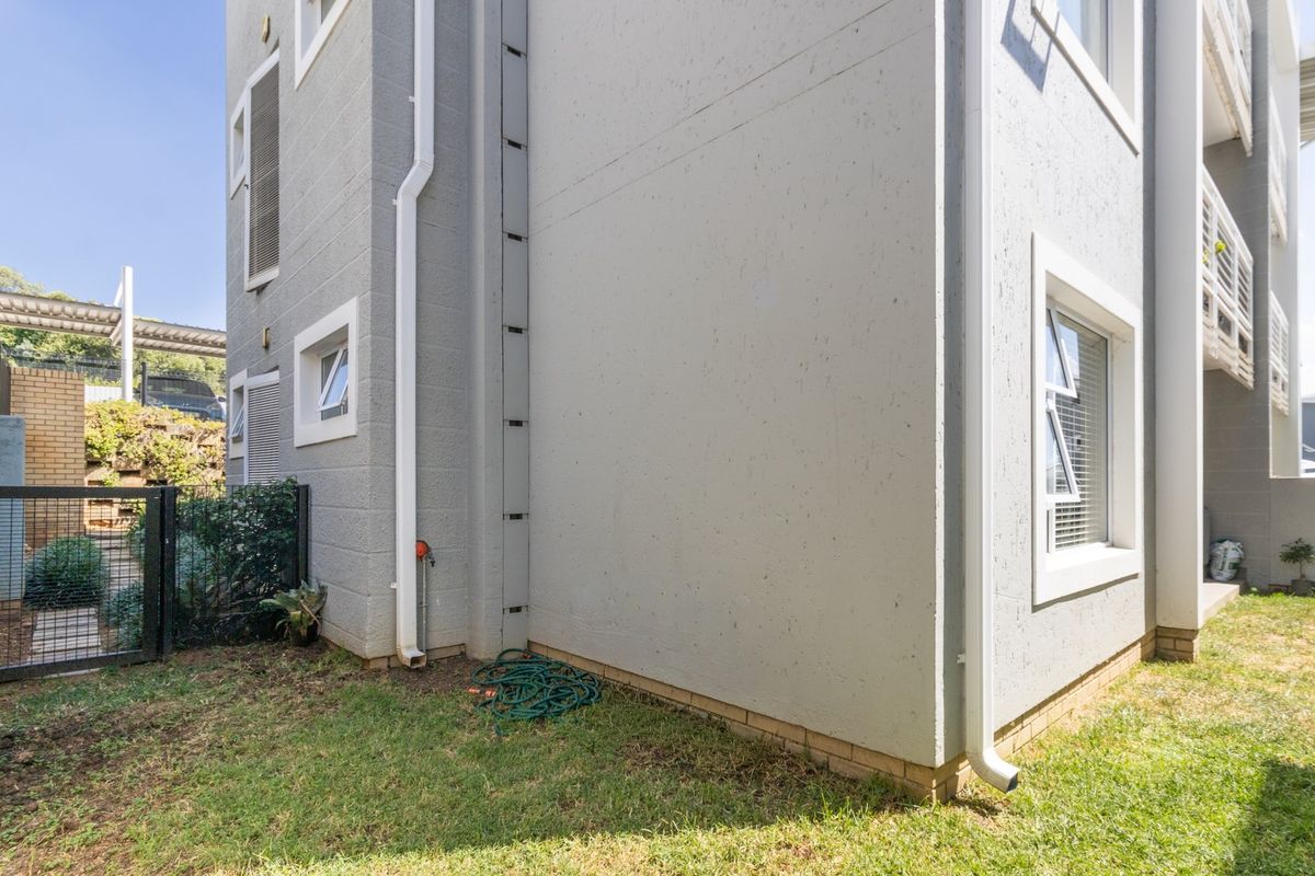 A view of the rear exterior facade of the apartment building, featuring plastered walls, downpipes, and casement windows overlooking a small garden area.