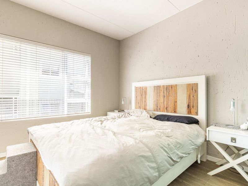 A well-lit bedroom featuring textured walls, laminate flooring, and venetian blinds, providing a neutral and comfortable living space.
