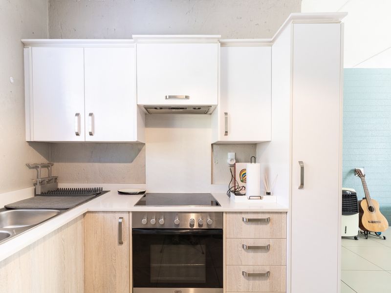 A modern, compact kitchen featuring light wood-grain lower cabinets, white upper cabinetry, stone countertops, and integrated stainless steel appliances.