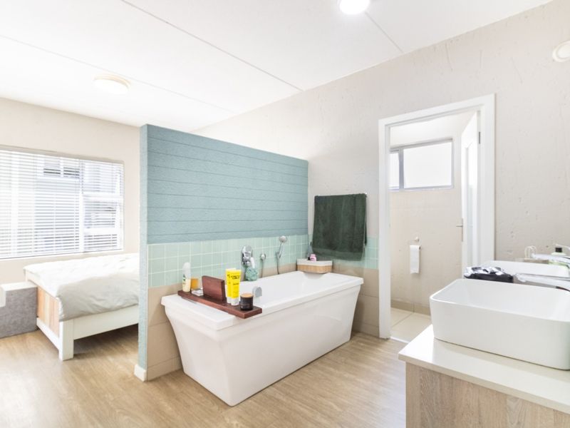 Open-plan bedroom featuring a modern freestanding bathtub, dual vanity sinks, and a decorative partition wall with tiled splashback.