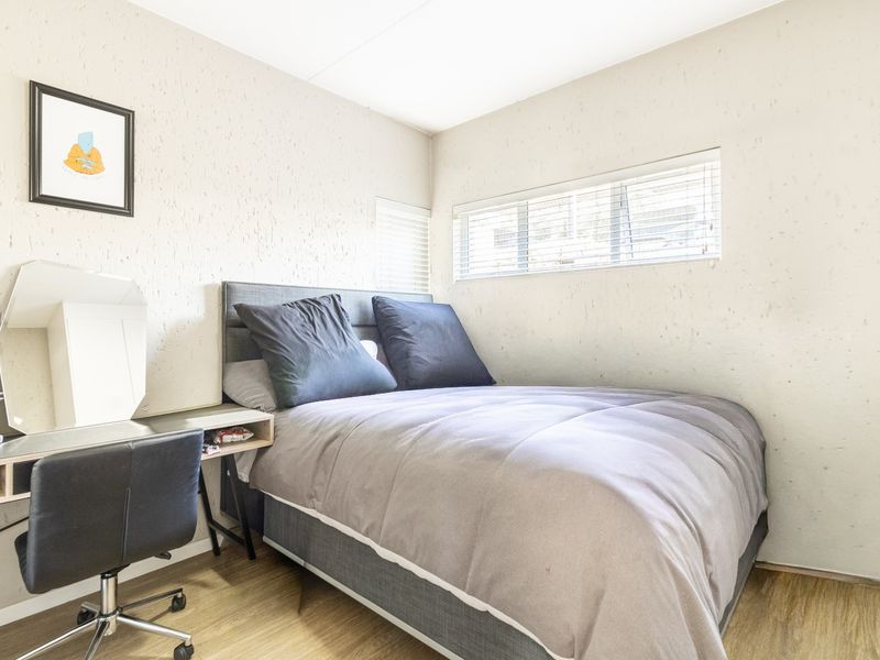 A compact bedroom featuring textured walls, laminate flooring, and horizontal window blinds, providing a functional and neutral living space.
