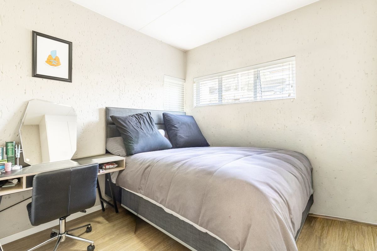 A compact bedroom featuring textured walls, laminate flooring, and horizontal window blinds, providing a functional and neutral living space.