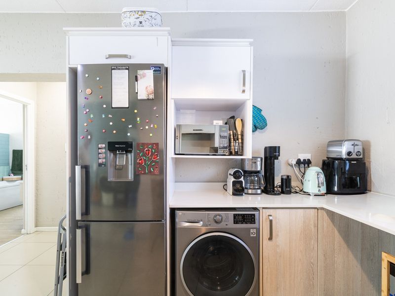 A functional kitchen area featuring built-in cabinetry, a countertop, a built-in microwave, and an integrated washing machine, with a view into the adjacent bathroom.