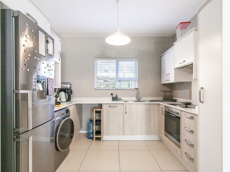 A functional kitchen featuring light wood-finish cabinetry, integrated oven and hob, stainless steel sink, and tiled flooring with ample storage space.