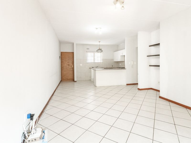 An open-plan living and kitchen area featuring tiled flooring, a breakfast counter, and built-in shelving, offering a bright and functional layout.