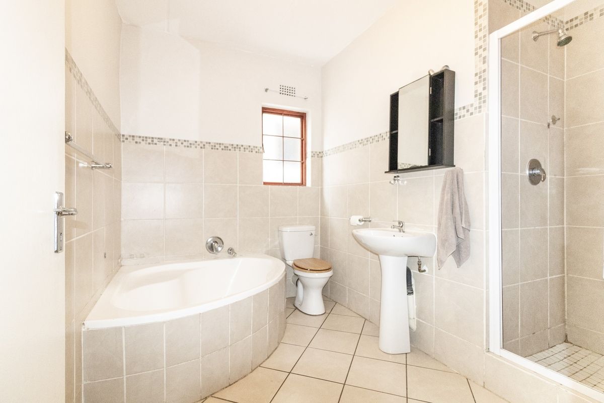 A functional bathroom featuring a corner bathtub, separate shower enclosure, pedestal basin, and toilet with neutral wall and floor tiling.
