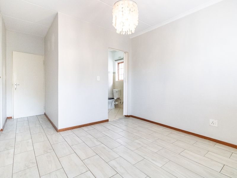 A bright, empty bedroom featuring neutral tiled flooring, clean white walls, and direct access to an en-suite bathroom.