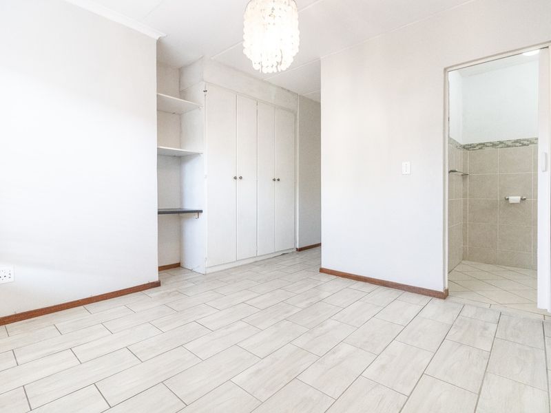 A bright, empty bedroom featuring neutral tiled flooring, built-in storage cupboards, and direct access to an en-suite bathroom.