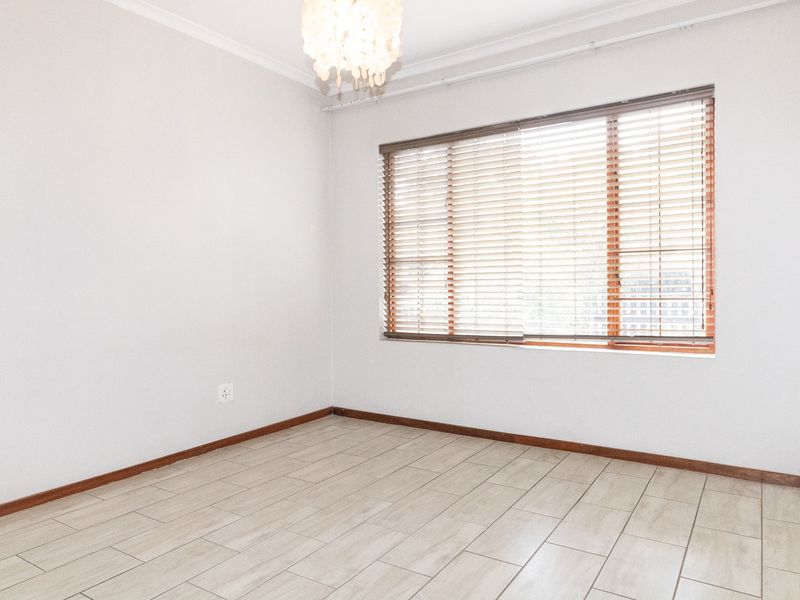 A bright, empty bedroom featuring neutral tiled flooring, clean white walls, and wooden venetian blinds, offering a versatile space ready for personalization.