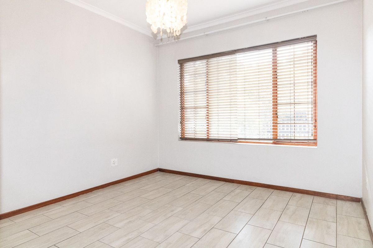 A bright, empty bedroom featuring neutral tiled flooring, clean white walls, and wooden venetian blinds, offering a versatile space ready for personalization.