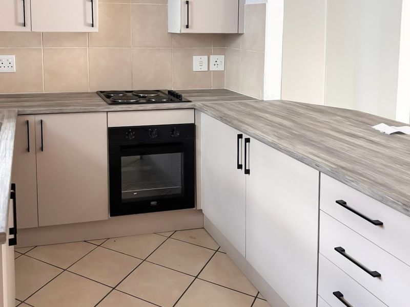 A clean, functional kitchen featuring built-in cabinetry, a modern electric hob, an integrated oven, and durable tiled flooring with a neutral backsplash.