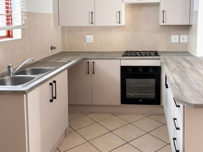 A clean, functional kitchen featuring modern cabinetry, laminate countertops, a built-in oven and hob, and neutral tiled flooring.