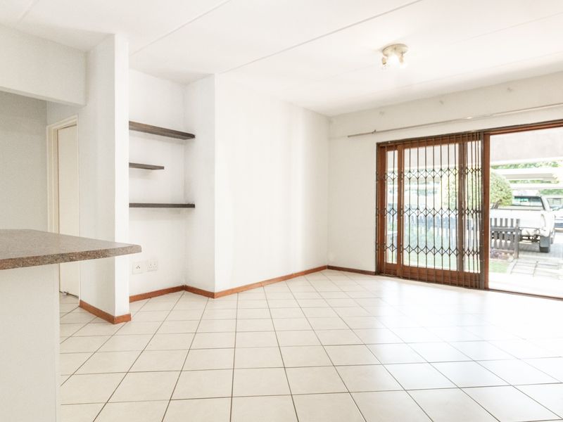 Bright open-plan living area featuring tiled flooring, built-in shelving, a breakfast bar, and sliding glass doors leading to the exterior.