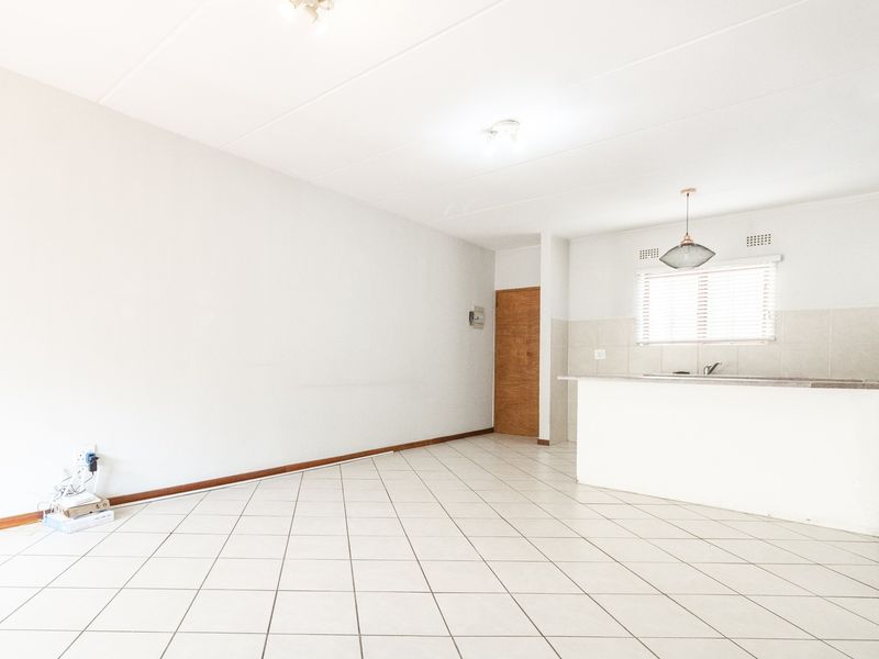 An open-plan living and kitchen area featuring neutral tiled flooring, a breakfast bar, and a functional kitchen layout with a sink and tiled backsplash.