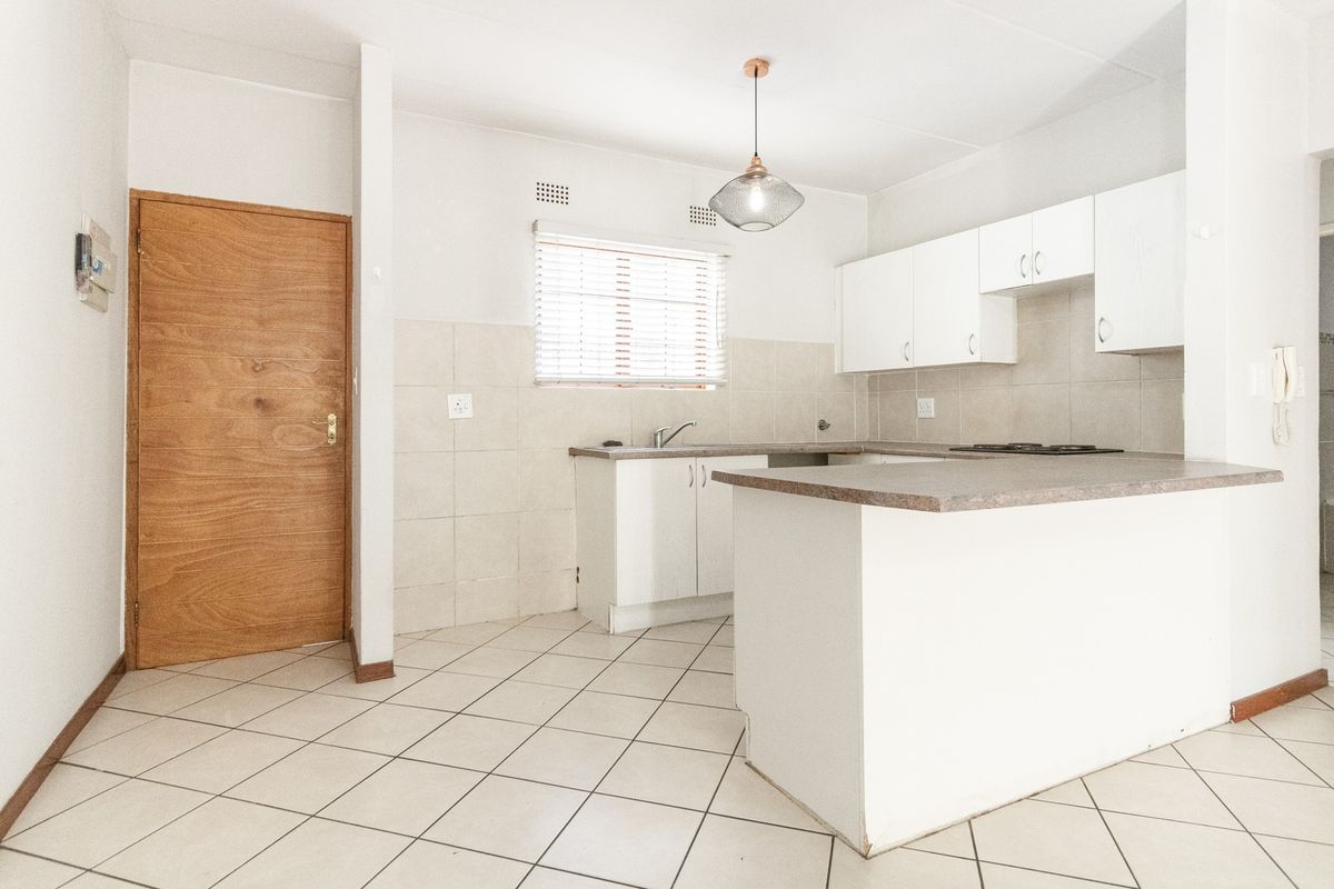 A functional, empty kitchen featuring white cabinetry, laminate countertops, tiled flooring, and a built-in hob, offering a clean canvas for potential updates.