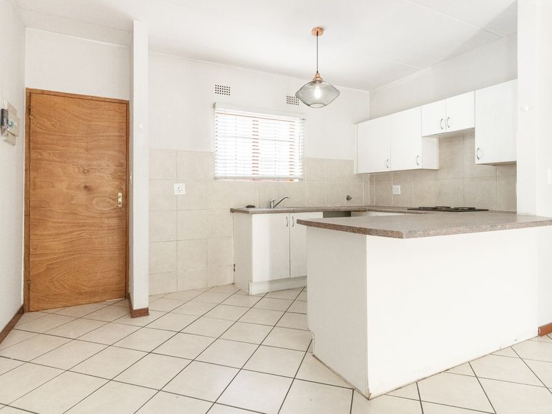 A functional, empty kitchen featuring white cabinetry, laminate countertops, tiled flooring, and a built-in hob, offering a clean canvas for potential updates.