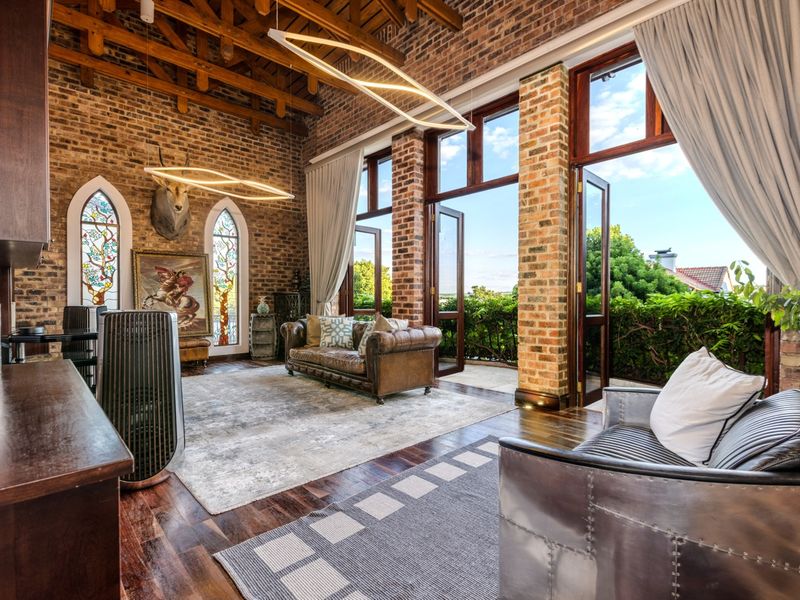 Spacious living room featuring exposed brick walls, high timber beam ceilings, hardwood floors, and large glass doors opening to an outdoor area.