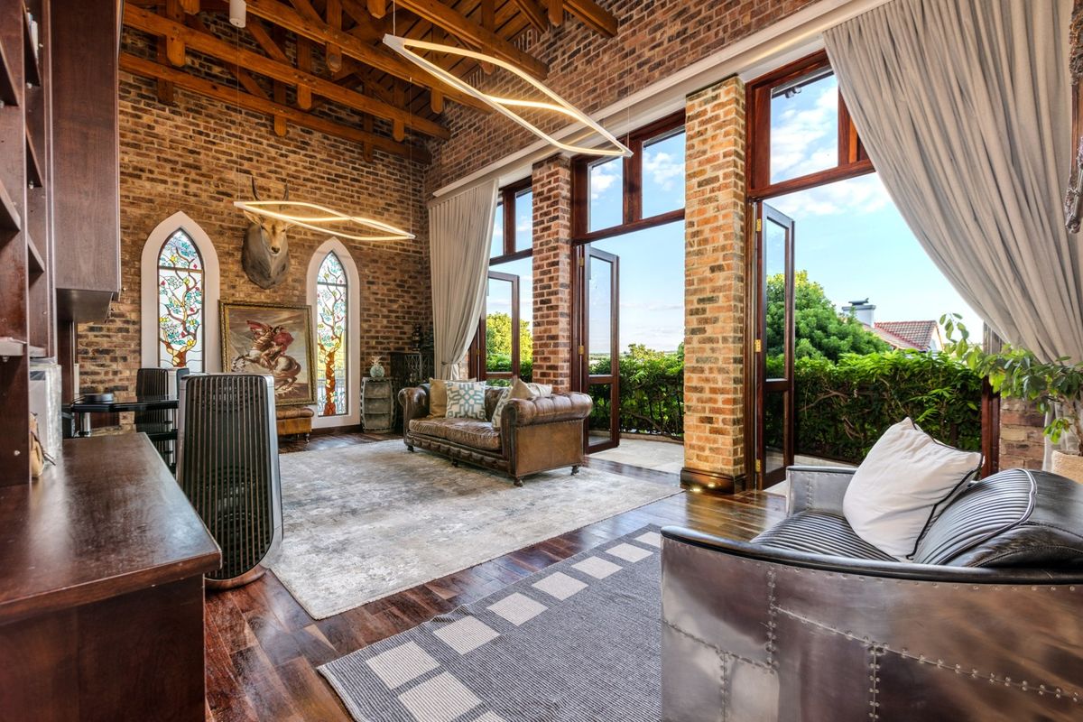 Spacious living room featuring exposed brick walls, high timber beam ceilings, hardwood floors, and large glass doors opening to an outdoor area.