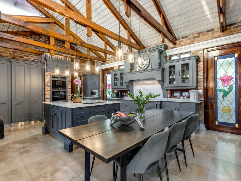 A high-end kitchen featuring exposed timber trusses, brick walls, a large central island with stone countertops, and elegant stained glass detailing.