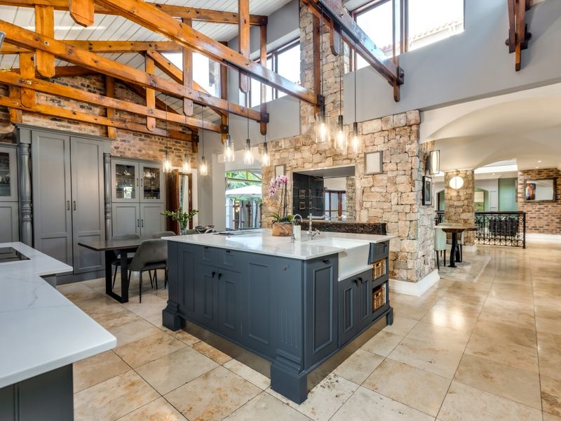A high-end kitchen featuring exposed timber trusses, a stone feature wall, a large central island with a farmhouse sink, and elegant cabinetry.