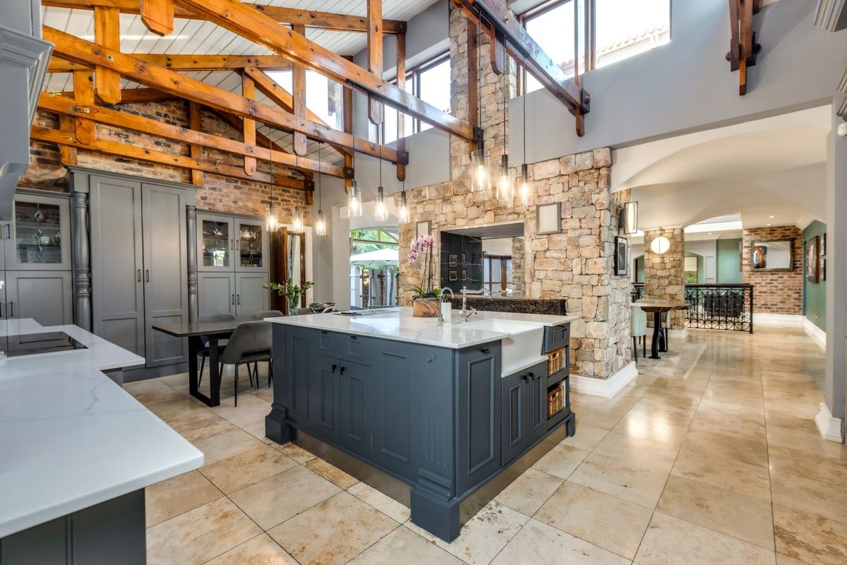 A high-end kitchen featuring exposed timber trusses, a stone feature wall, a large central island with a farmhouse sink, and elegant cabinetry.