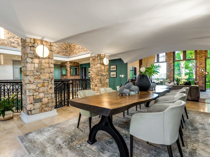 Spacious open-plan living and dining area featuring striking stone-clad columns, vaulted ceilings, exposed brickwork, and elegant wrought iron detailing.