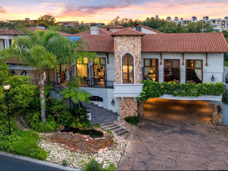 Stunning multi-level residence featuring stone accents, terracotta roof tiles, a paved driveway, and a beautifully landscaped front garden with a water feature.