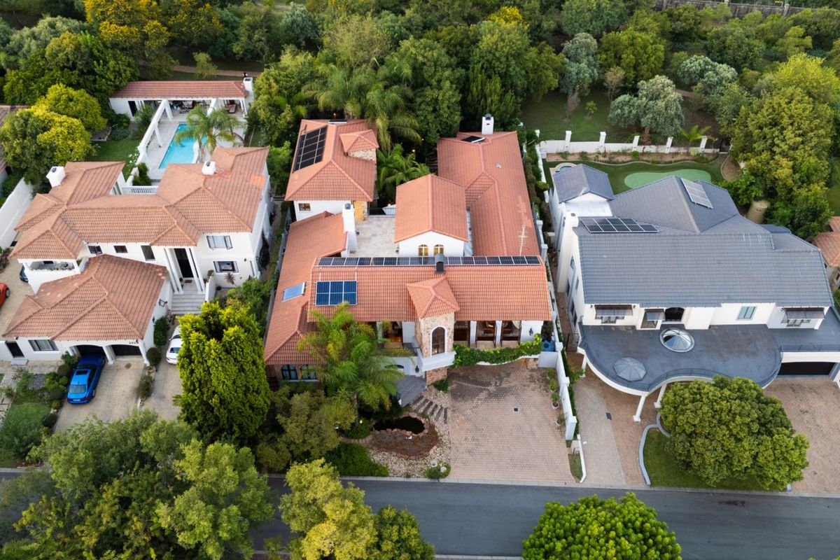 Aerial view of a residential property featuring a tiled roof with integrated solar panels, a paved driveway, and established garden surroundings.