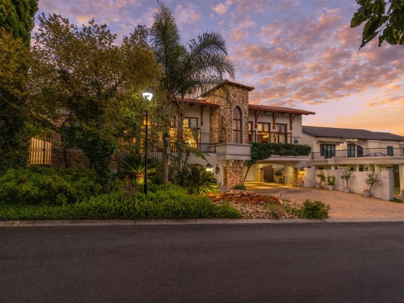 Stunning multi-story residence featuring stone facade, terracotta roof tiles, wrought iron balconies, and a beautifully landscaped front garden with paved driveway.