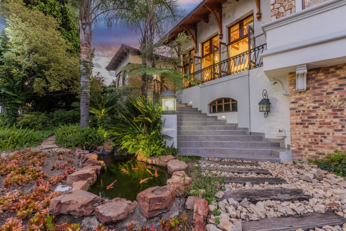 A beautifully landscaped rear garden featuring a stone-lined koi pond, a grand stone staircase leading to an elevated balcony, and charming architectural stone detailing.