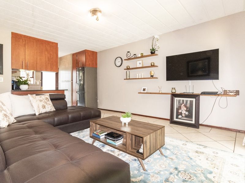 Open-plan living area featuring tiled floors, floating wall shelving, and an integrated kitchen space with wooden cabinetry.