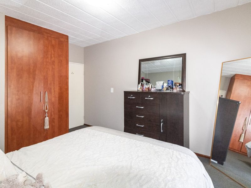 A bedroom featuring a built-in wooden wardrobe and a textured ceiling, providing functional storage space within the room.
