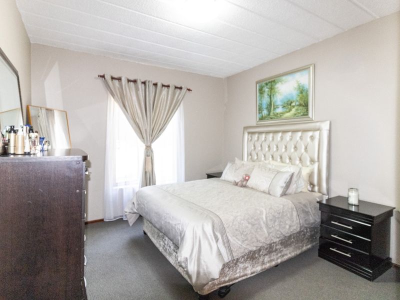 A well-lit bedroom featuring neutral wall tones, carpeted flooring, and a textured ceiling, providing a comfortable and functional living space.