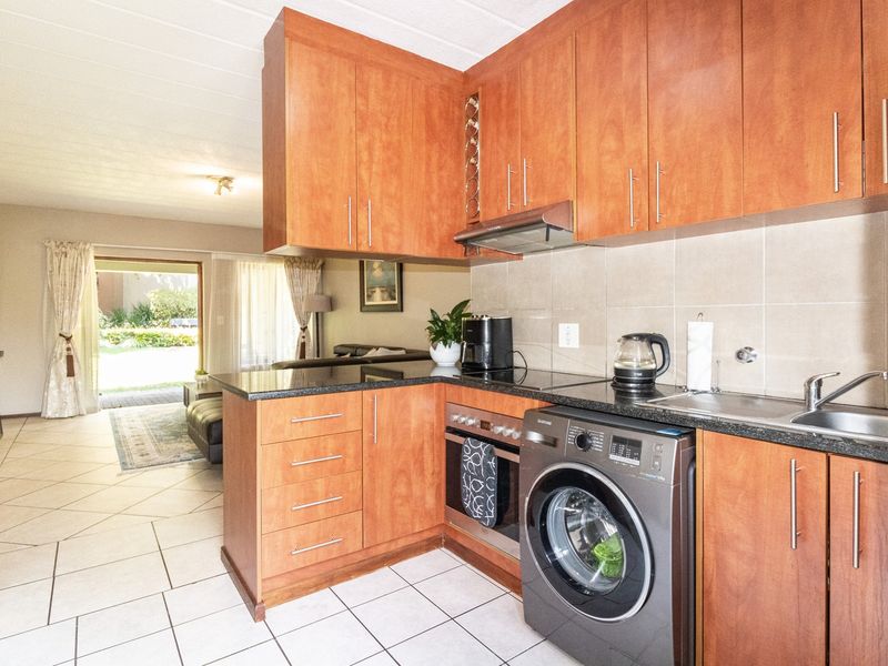 Open-plan kitchen featuring wood-finish cabinetry, granite countertops, and integrated appliances, flowing seamlessly into the living area with direct access to the outdoor space.